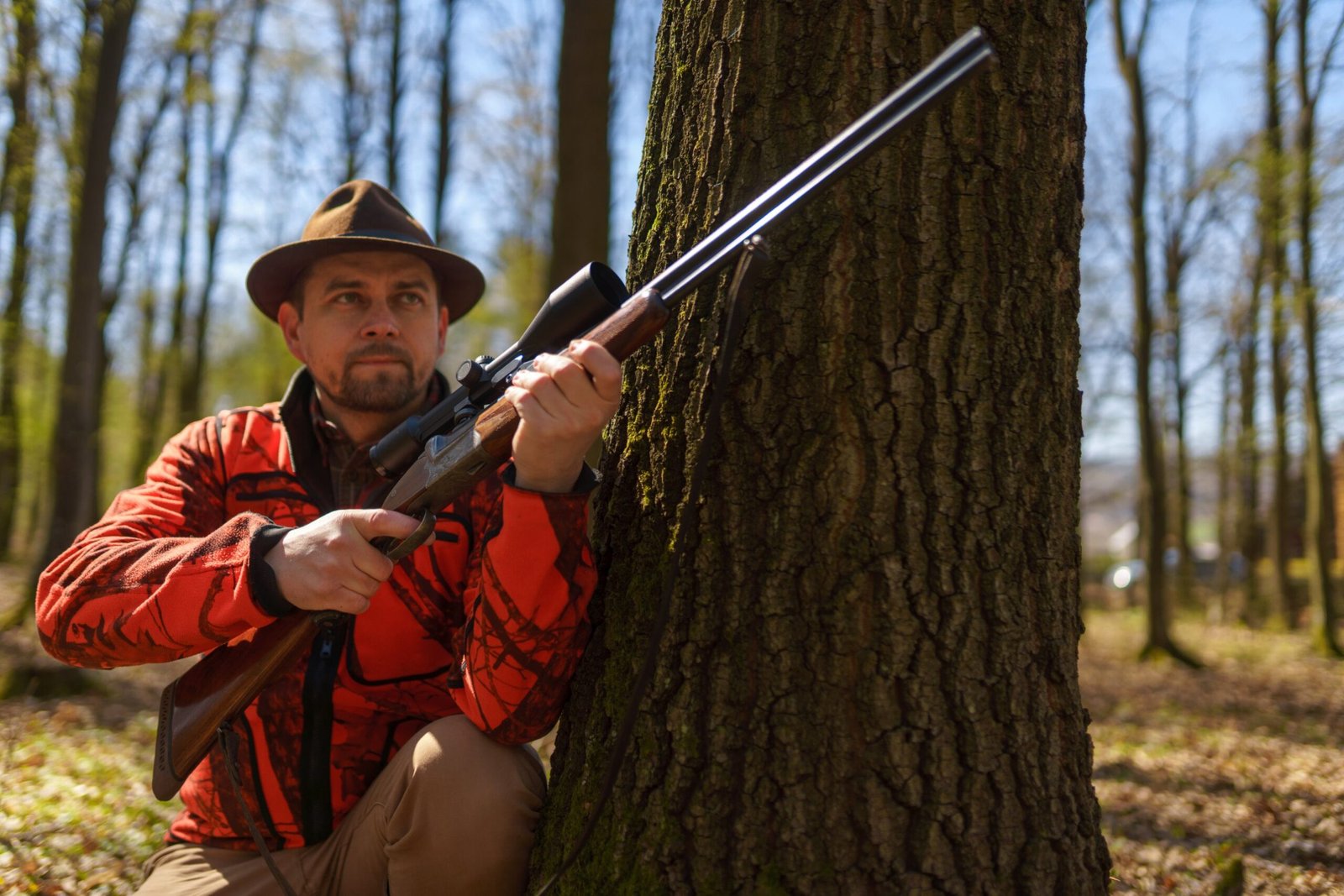 Chasseur en veste orange posté contre un arbre