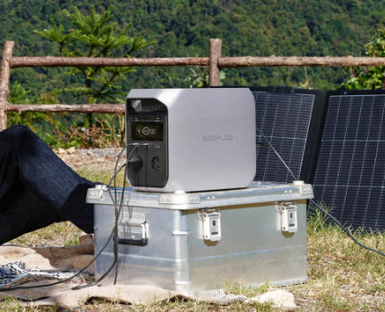 Station EcoFlow posée sur une caisse en aluminium, à côté de panneaux solaires, devant une vallée boisée