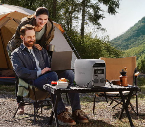 Deux campeurs devant leur tente, un ordinateur portable relié à la station EcoFlow posée sur une table de camping
