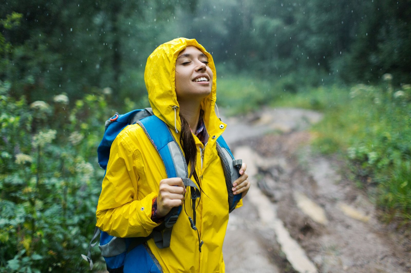 Randonneuse souriante sous la pluie, capuche de sa veste jaune relevée