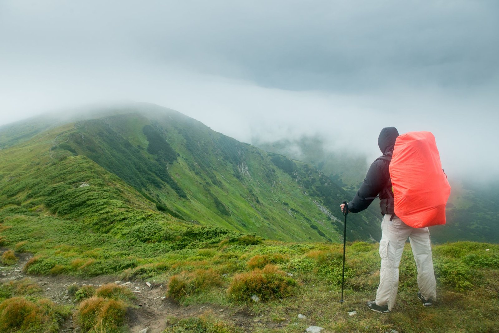 Randonneur avec une housse de sac rouge face à une crête dans le brouillard
